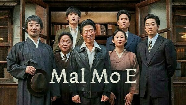 A promotional image for the Korean film Mal Mo E, featuring seven characters standing in front of a wooden building with bookshelves. They are dressed in early-to-mid 20th century Korean and Western-style clothing. The man in the center, wearing a leather jacket, smiles warmly, while others stand with serious or calm expressions. The film title "Mal Mo E" is displayed prominently across the image.