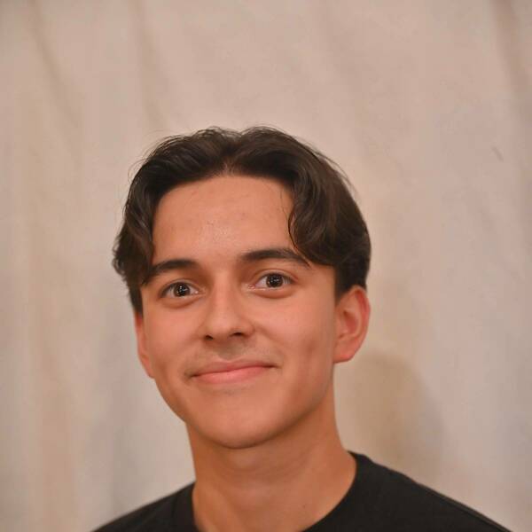 Young man with dark hair and wearing a dark shirt.  He is smiling and looking directly into the camera.