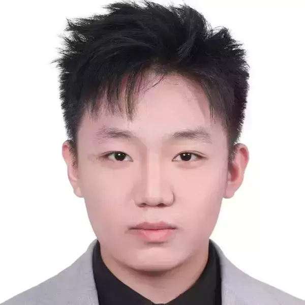 Young man with spiky black hair, wearing a black collared shirt and grey suit jacket, looking forward with a neutral expression.